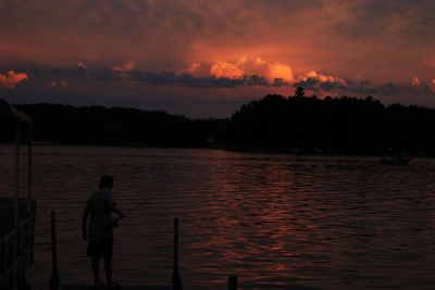 Silhouette man fishing in sea against sunset sky