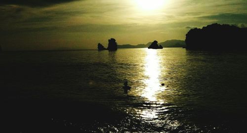 Silhouette people on sea against sky during sunset