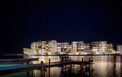 Illuminated buildings by sea against sky at night