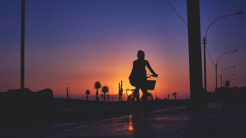 Silhouette woman on street against orange sky