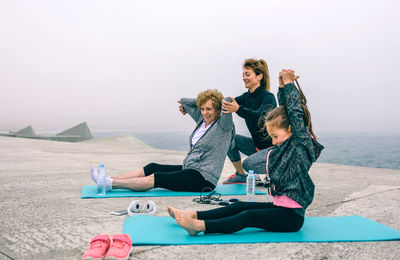 Mature woman with daughter and granddaughter exercising by sea on walkway