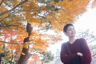 Low angle view of young woman standing in park during autumn