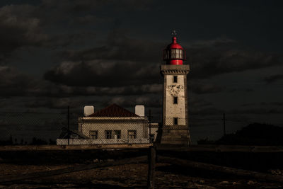 Lighthouse by building against sky at night