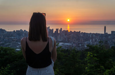 Rear view of woman standing against sky during sunset