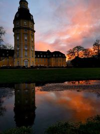 Built structure by lake and buildings against sky during sunset