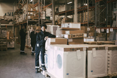 Smiling female entrepreneur leaning on box containers at distribution warehouse