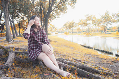 Young woman sitting on tree against plants