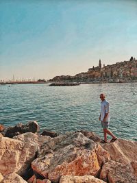 Rear view of man standing on rock by sea against sky