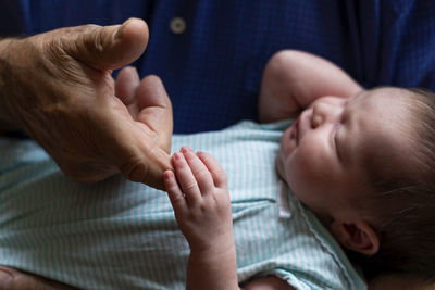 Sleeping newborn baby holding grandfathers finger