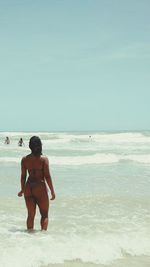 Rear view of shirtless man standing on beach against clear sky