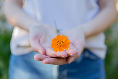 Young woman is holding an orange flower, sharing