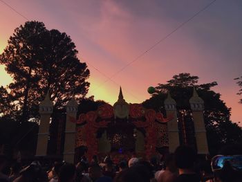 People by trees against sky during sunset