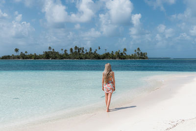 Rear view of woman standing at beach against sky