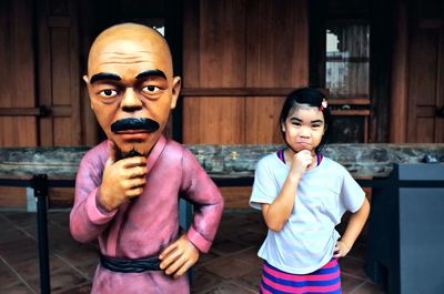 Portrait of cute smiling girl standing by statue against house