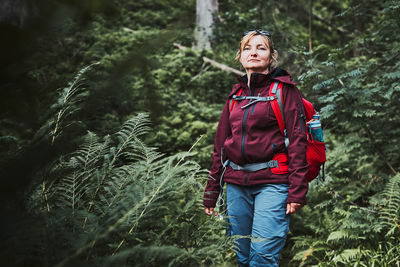 Woman with backpack hiking in forest, actively spending summer vacation close to nature