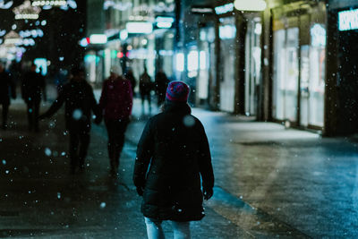 Rear view of woman walking on street during winter