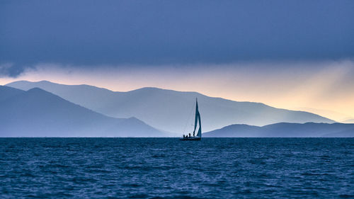 Sailboat sailing on sea against mountains during sunset