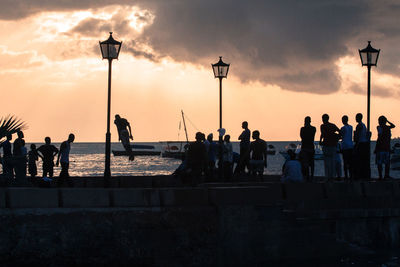 People looking at man jumping into sea against sky during sunset