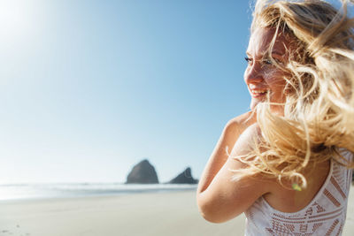 Close-up of smiling young woman standing at beach against clear sky