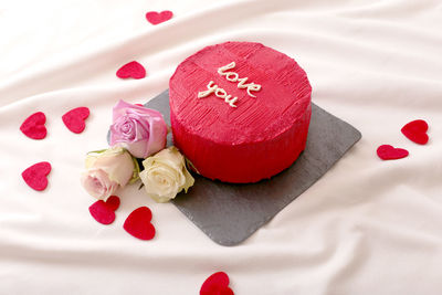 Round red bento cake, hearts and roses lie on white bed in daylight