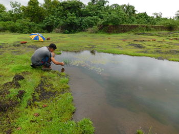 Full length of boy photographing by pond on field