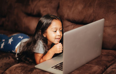 Cute girl using laptop while lying on sofa at home