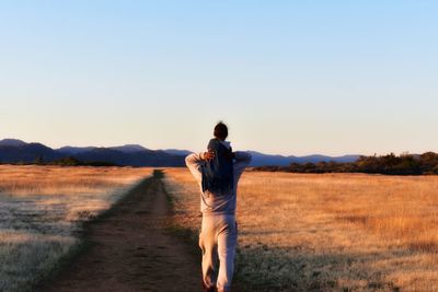 Rear view of man standing on field against clear sky