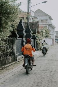 Rear view of man riding motor scooter on street