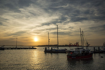 Sailboats moored on sea against sky during sunset