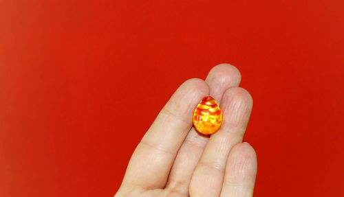 Cropped image of person holding easter egg decoration against red background