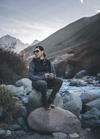 Young man sitting on rock against mountains