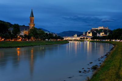 Illuminated buildings by lake against sky