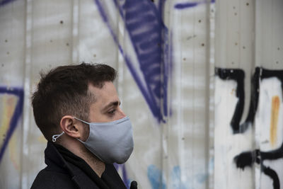 Side view of man wearing mask against wall outdoors