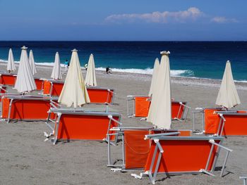 Chairs and tables on beach by sea against sky