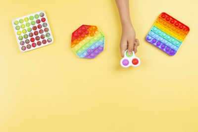 Kid hand holding pop it fidget toy on pastel yellow background. push pop-it fidgeting game. top view
