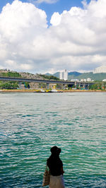 Woman by river against sky in city