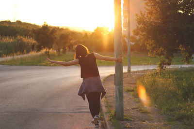 Rear view of playful young woman holding pole by road