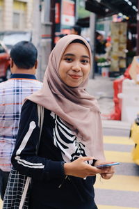 Portrait of smiling woman using phone while standing on road