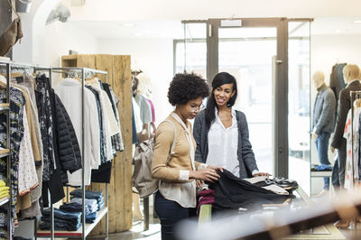 Friends talking while checking shirts at store on sunny day