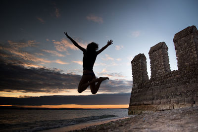 Silhouette man jumping at beach against sky during sunset