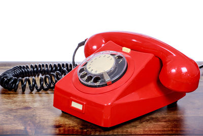 Close-up of red rotary phone on wooden table against white background