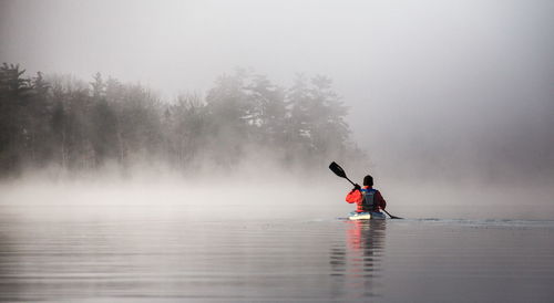 Rear view of man kayaking in river during foggy weather