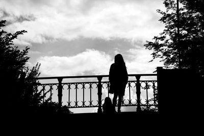 Silhouette woman standing by railing against sky