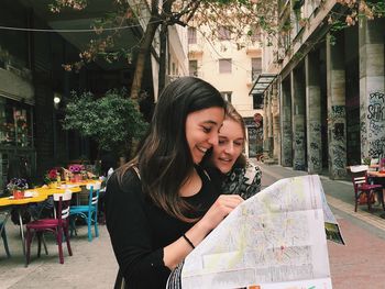 Happy female friends looking on map in city