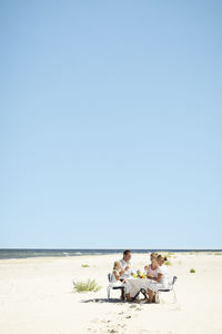 People sitting on beach against clear sky