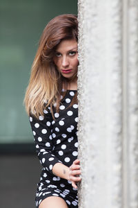 Portrait of young woman peeking by wall