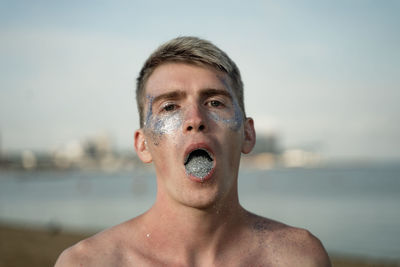 Portrait of young man with glitter in mouth against sea