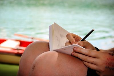 Midsection of woman writing on book by sea 