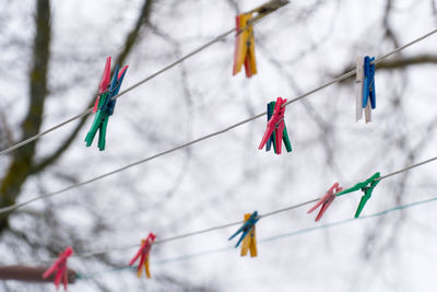 Low angle view of multi colored clothespins hanging on clotheslines against sky