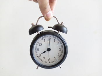 Cropped hand of person holding alarm clock against white background
